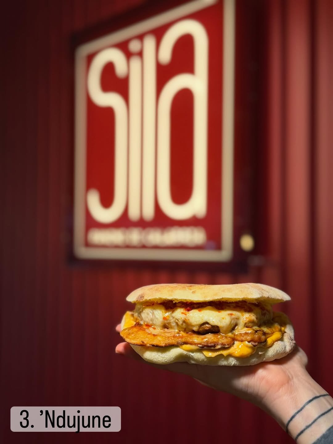 'Ndujune panino in front of the red Sila board