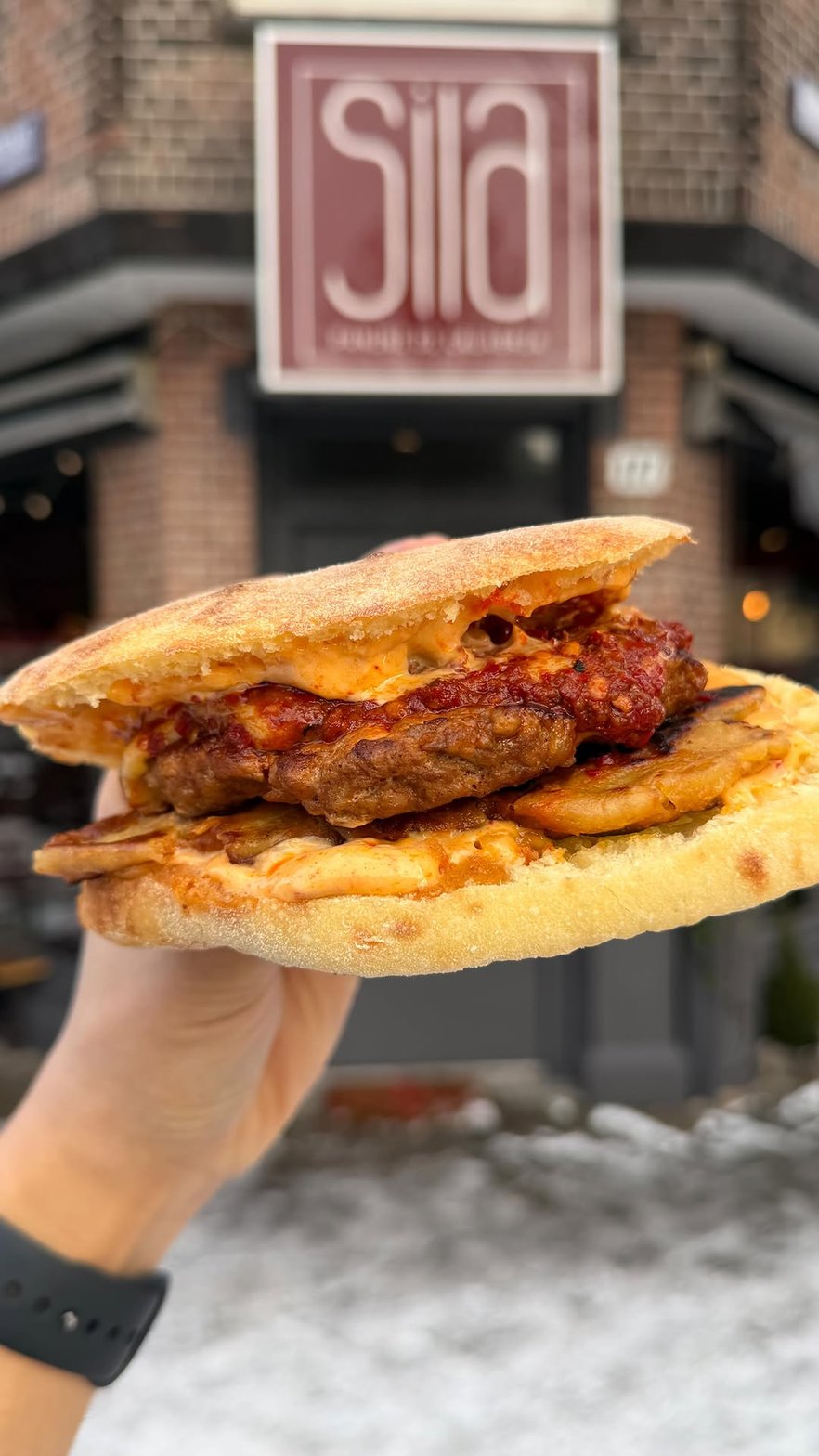 A Sila panino in front of the bordeaux facade of Sila on Van Woustraat in Amsterdam